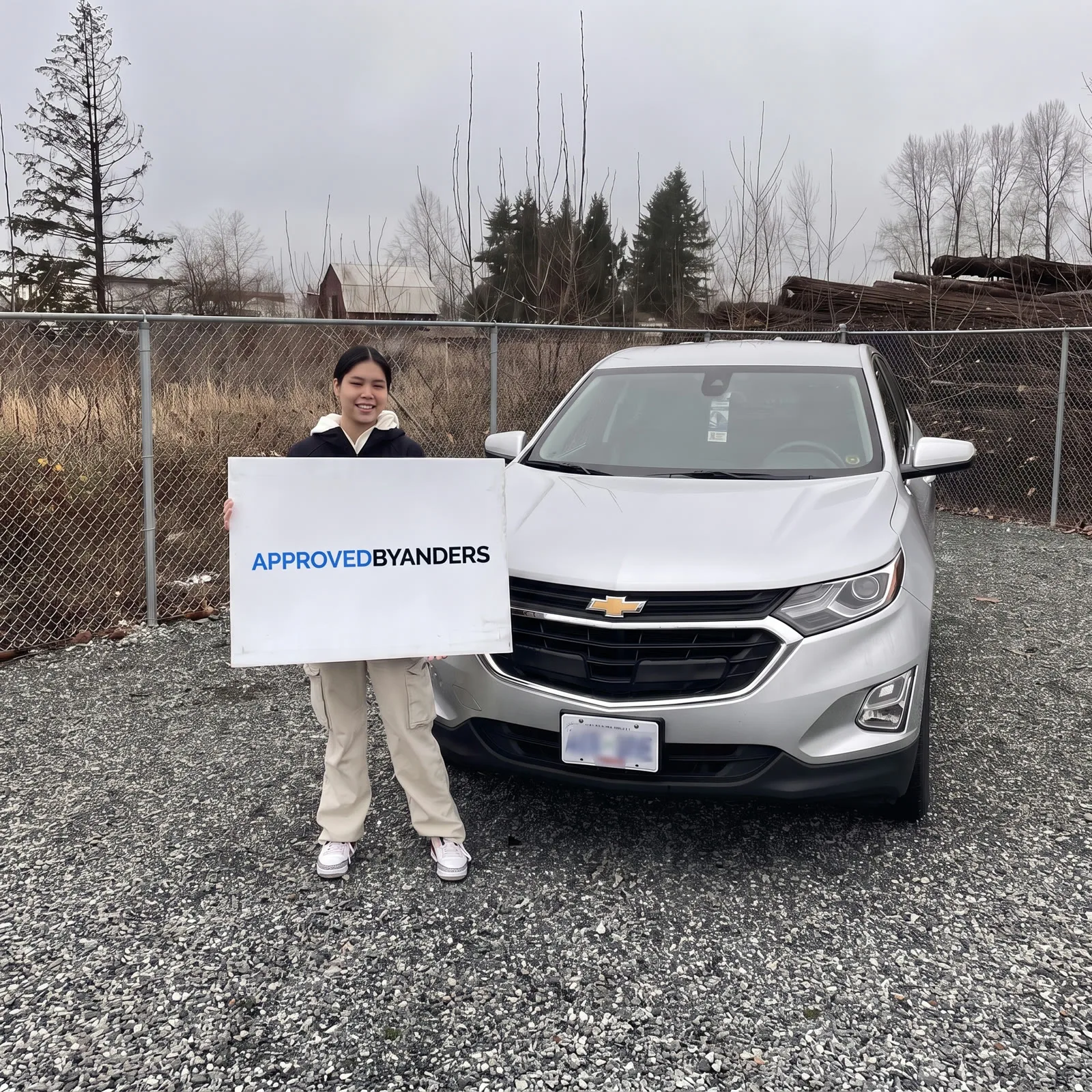 Woman holding a large "Thanks Anders!" board beside her silver Chevrolet Equinox