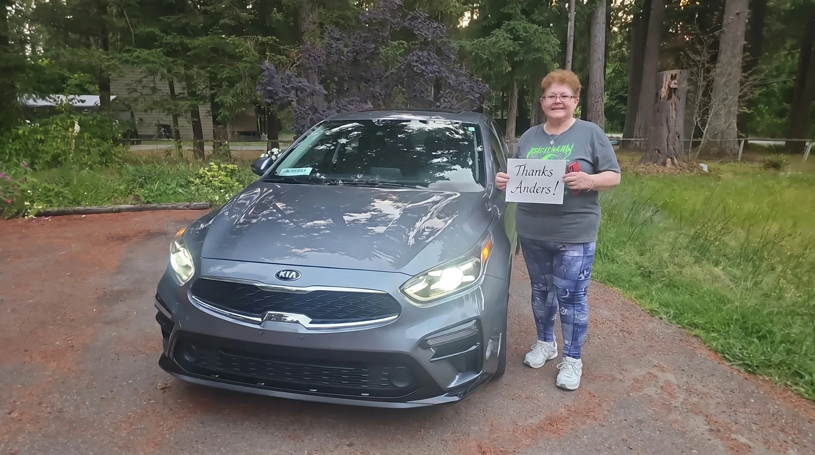 Woman with her grey Kia Forte on a forest driveway