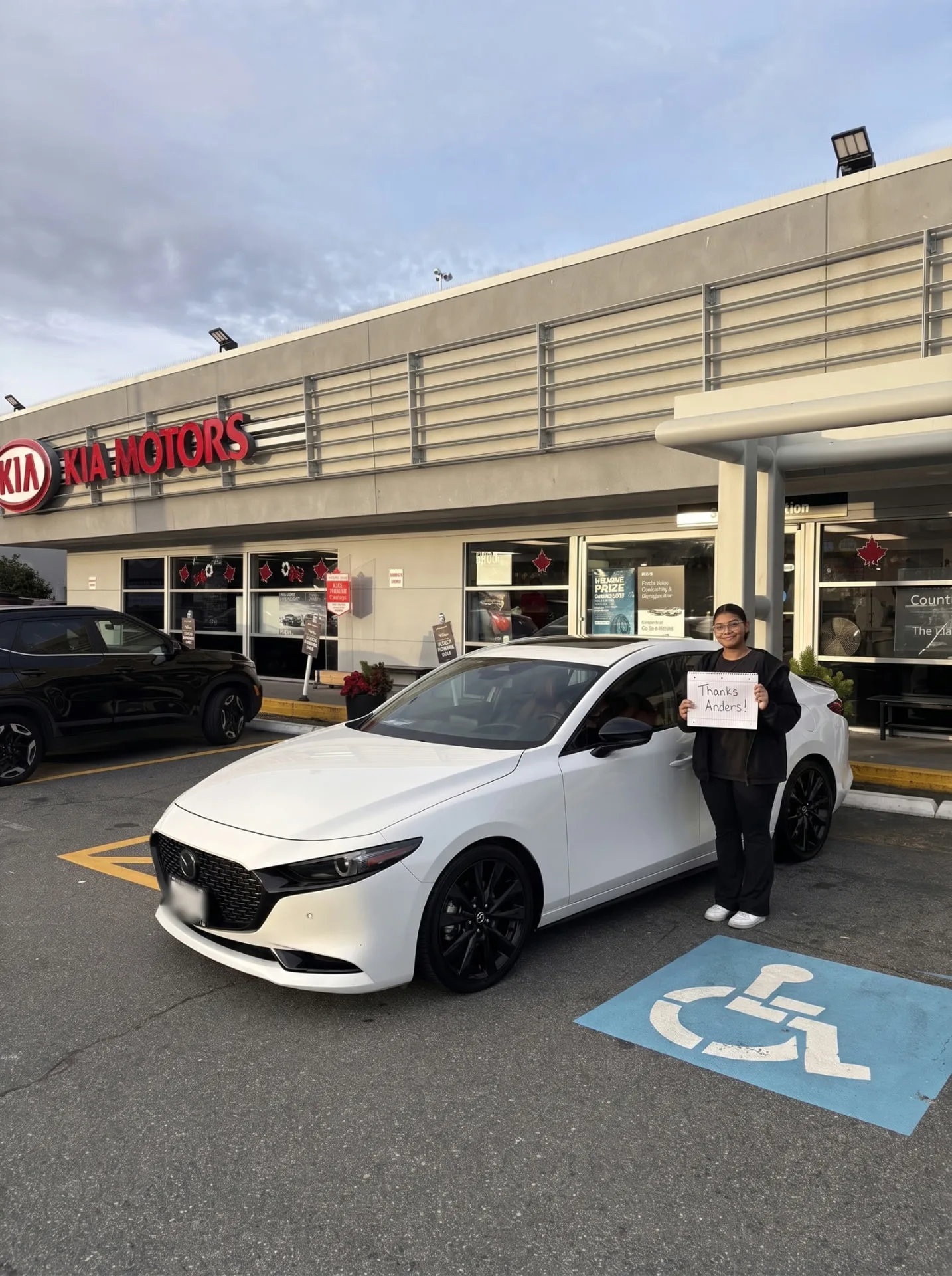 Woman with her white Mazda3 at the Kia store