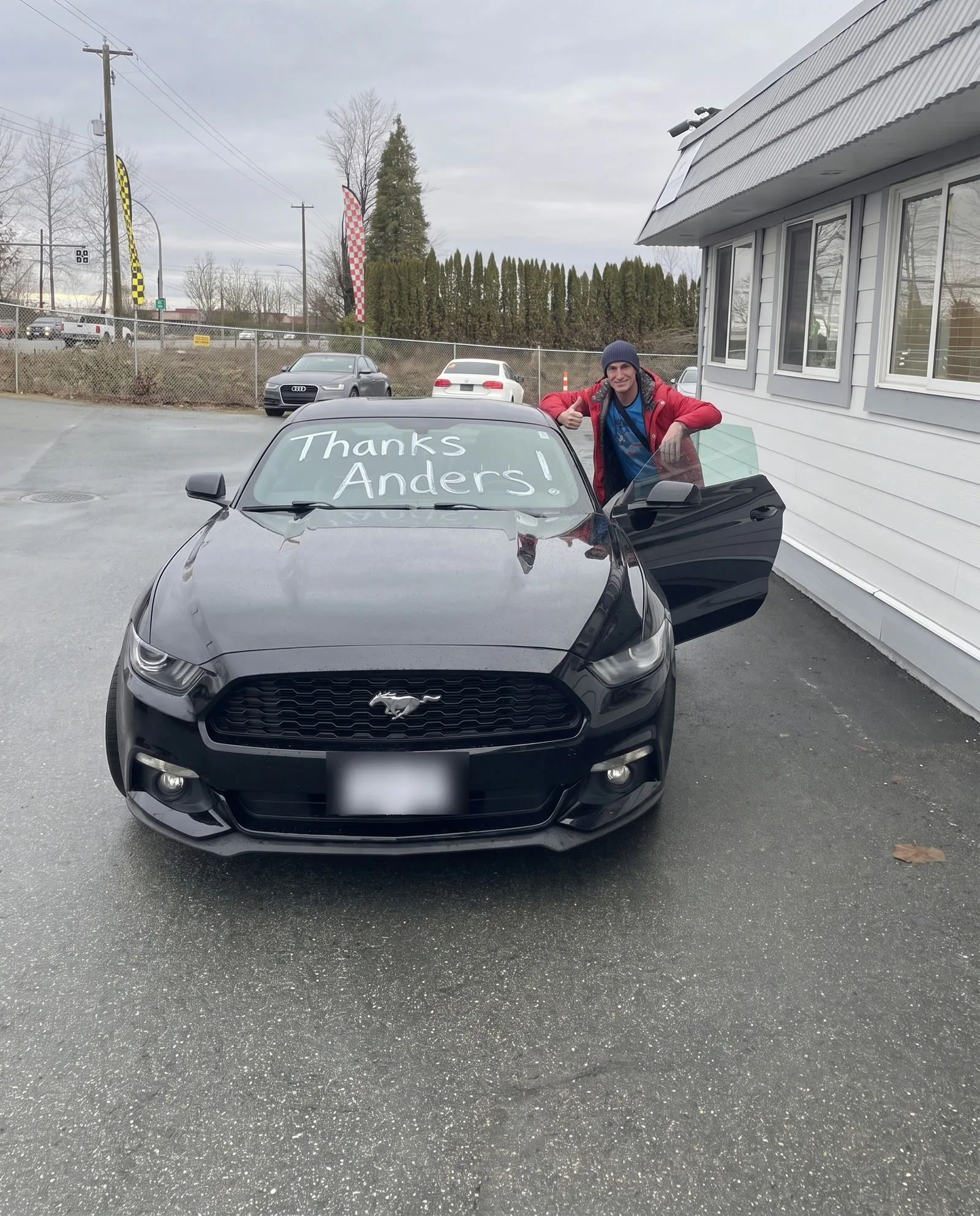 Man giving a thumbs-up behind the door of his black Ford Mustang