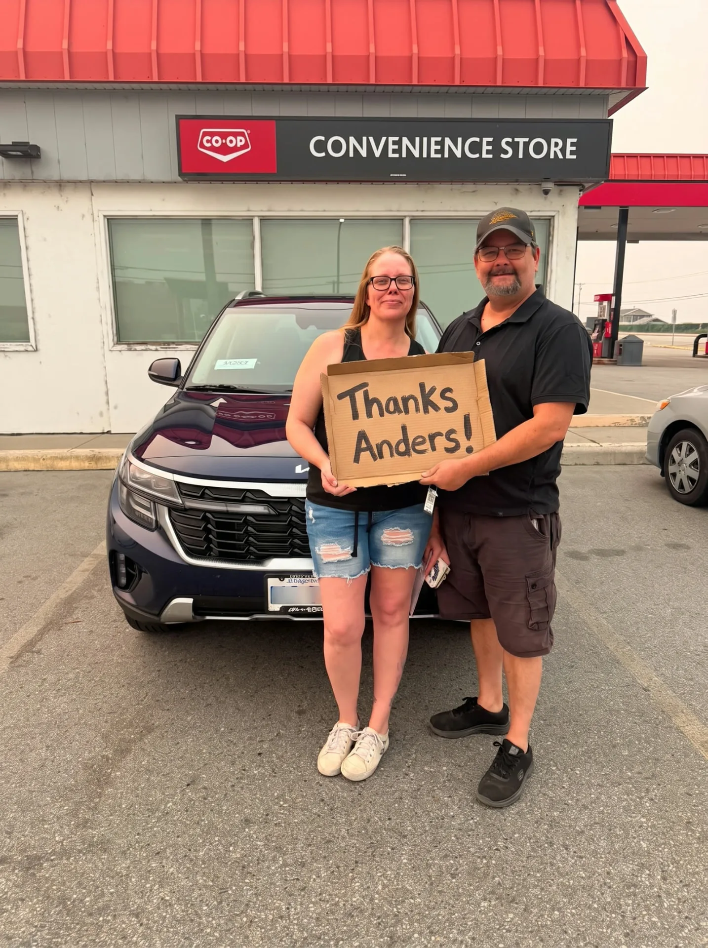 Couple with their blue Kia Seltos, holding the sign together