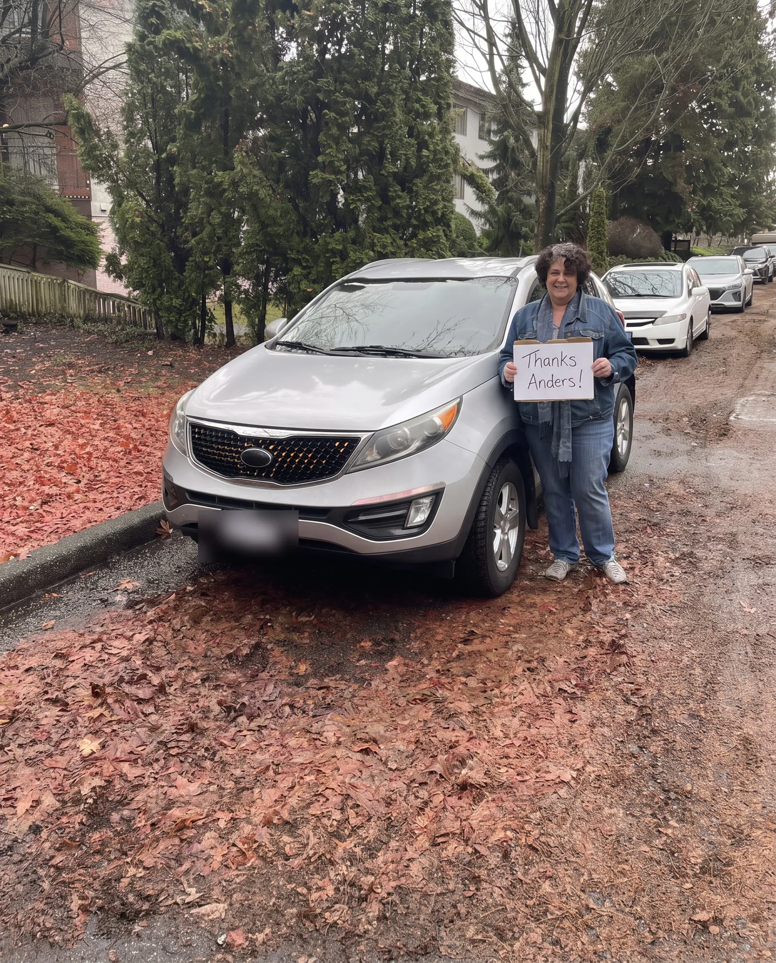 Woman with her silver Kia Sportage on a leaf-covered street